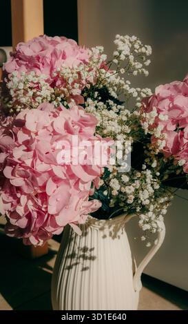 Élégant bouquet d'hortensia rose et de fleurs blanches du souffle de bébé disposées dans une cruche en céramique crème sous la lumière naturelle douce du soleil Banque D'Images