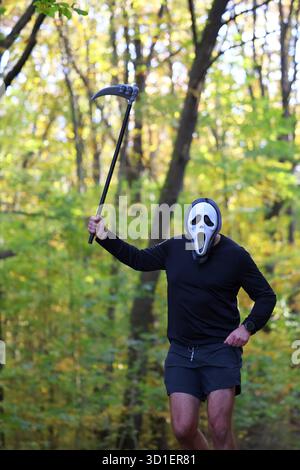 Halloween Ghostface Runner avec Scythe sur un sentier forestier d'automne Banque D'Images