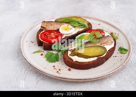 Sandwichs sur pain de seigle, avec sprats, œufs de caille, tomates fraîches et concombre mariné, apéritif, petit déjeuner, fait maison Banque D'Images