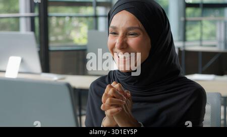 Islamique ethnique heureuse femme d'affaires gagnant en ligne célébration de réalisation femme d'affaires dans le hijab dans le bureau gagner victoire ordinateur Internet bonne nouvelle Banque D'Images