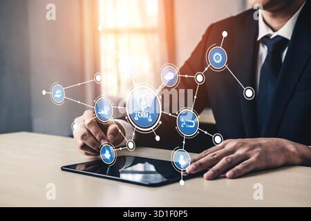 Un professionnel interagit avec une tablette présentant des connexions numériques et des icônes CRM. Cette image symbolise la technologie moderne pour la commercialisation d'un Banque D'Images
