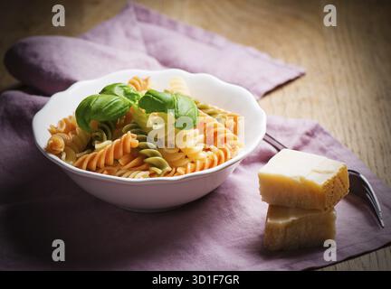 Macaronis en spirale cuits avec basilic dans une assiette sur une serviette et une vieille table en bois avec du fromage à pâte dure Banque D'Images