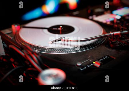 Vue rapprochée de la platine DJ et du disque vinyle sous l'éclairage rouge du club avec accent sur le tonearm et les groove. Banque D'Images