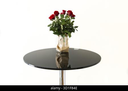 Bouquet de roses rouges dans un vase en papier gris sur table en verre noir isolé Banque D'Images