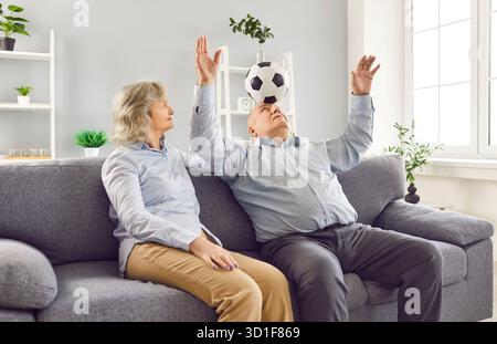 Couple senior retraité assis sur le canapé dans le salon à la maison et s'amuser avec le ballon de football. Banque D'Images