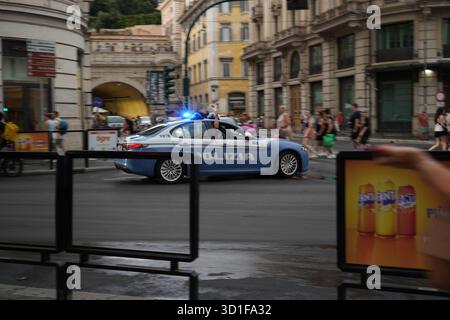 Voiture Polizia accélérée avec sirène clignotante. Le bras de l'officier s'étend de la fenêtre tenant une palette blanche de circulation, indiquant un mouvement urgent. Banque D'Images