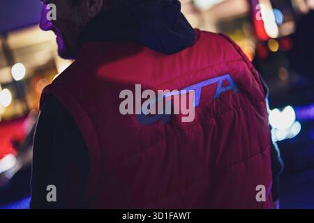 Este, italie 28 octobre 2025 : personne vue de derrière dans un gilet rouge gta, debout contre des lumières bokeh nocturnes urbaines floues suggérant une vie nocturne cyberpunk Banque D'Images