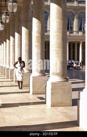 Jeune Noire posant pour des photos dans une robe blanche aux colonnes du Palais Royal à Paris, France - mode, influenceur Banque D'Images