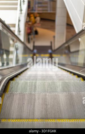 Vue rapprochée d'un escalier roulant d'un centre commercial britannique, depuis la marche supérieure jusqu'à l'étage inférieur lointain. Banque D'Images