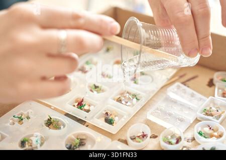 Mains versant de la résine dans des moules pour la fabrication artistique de bijoux à l'atelier d'artisanat. Banque D'Images