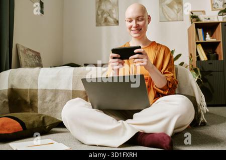 Jeune femme adulte avec Alopecia Sitting Cross Legged à l'aide d'un smartphone Banque D'Images