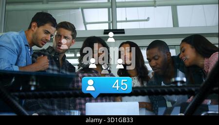 Six collègues se penchant sur l'ordinateur portable sur le bureau dans le bureau, montrant des icônes de médias sociaux, bulle bleue 45 Banque D'Images