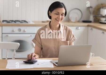 Femme âgée souriante gérant les finances personnelles sur le lieu de travail de cuisine à domicile Banque D'Images