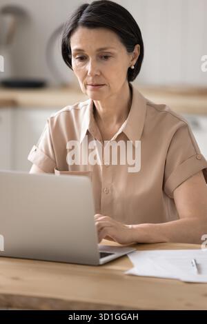 Femme d'affaires plus âgée sérieuse travaillant à la maison avec un cahier et des papiers Banque D'Images