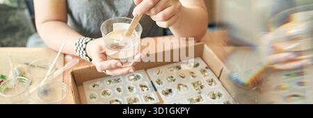 Jeune femme créant des bijoux en résine diy avec des outils de moule et de mélange. Banque D'Images