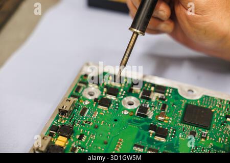 Une personne soude méticuleusement une carte mère à l'aide d'un fer à souder, en se concentrant sur le placement précis des composants électroniques Banque D'Images