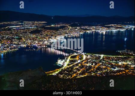 Une vue nocturne époustouflante de Tromso, en Norvège, illuminée par des lumières, avec un port et un pont qui s'étendent sur l'eau, au sommet de Storsteinen Banque D'Images