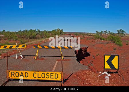 Route endommagée de l'Outback en Australie avec des fissures et de l'érosion, marquée par des panneaux « route fermée » dans un paysage désertique rouge. Banque D'Images