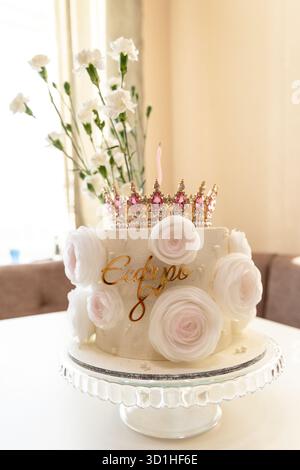 Un beau gâteau de couleur crème orné de roses roses et d'une couronne pétillante, parfait pour une célébration. Banque D'Images