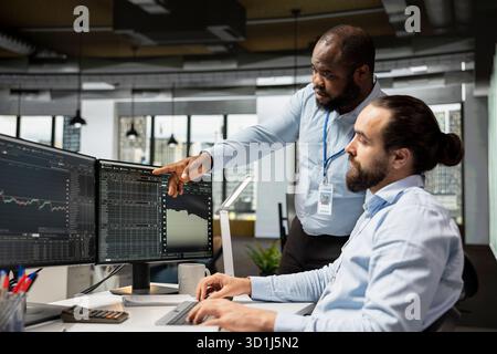 Équipe d'analystes de risque utilisant la plate-forme de trading sur PC pour examiner les signes de volatilité boursière. Des collègues de la firme d'accessoires de travail d'équipe analysent les rapports de performance du portefeuille, vérifient les risques financiers Banque D'Images
