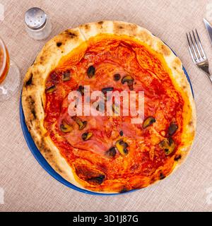 Sur l'assiette est une petite pizza ronde sur une fine pâte de levure avec des tranches de jambon et des morceaux de champignons. Banque D'Images
