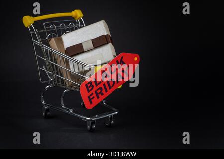 Chariot miniature transportant des cadeaux emballés et une étiquette de vendredi noir, symbolisant la frénésie du shopping pendant les soldes Banque D'Images