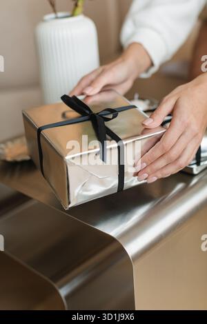 Gros plan d'une jeune femme assise sur un canapé déballant des cadeaux de Noël sur une table basse Banque D'Images