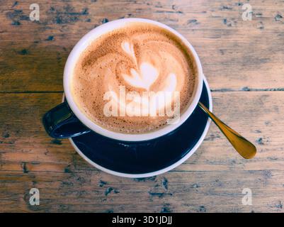 Café blanc plat dans une tasse en porcelaine avec un motif de fleurs fabriqué à partir de mousse de lait vapeur (micromousse) versé dans un espresso, également connu sous le nom de latte art. Banque D'Images