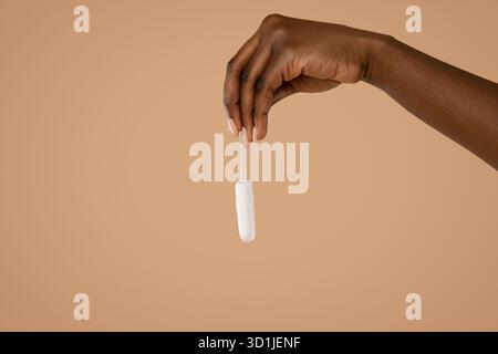 Femme noire tient tampon sur un fond beige mettant en valeur la sensibilisation à la santé menstruelle Banque D'Images