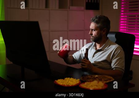 Homme d'affaires manger de la pizza en heures supplémentaires. Homme occupé des années 50 mangeant le dîner et travaillant en ligne au bureau de nuit. Entrepreneur travaille tard dans la nuit tout en profitant d'un Banque D'Images