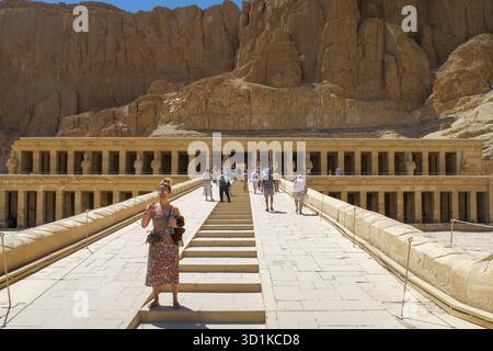 Touristes visitant l'ancien temple mortuaire d'Hatshepsout avec une architecture monumentale en pierre dans un cadre de montagne désertique, Egypte Banque D'Images