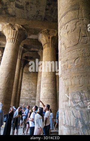 Touristes explorant l'intérieur d'un ancien temple égyptien d'Edfou avec des colonnes massives sculptées de hiéroglyphes et de reliefs pharaoniques, Egypte Banque D'Images