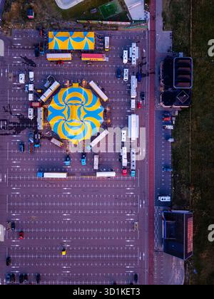 Vue aérienne de la configuration vibrante de cirque dans le parking tente en spirale jaune bleu entouré de remorques et de tentes plus petites, mettant en valeur Banque D'Images