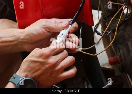 Gros plan d'une prise électrique en main, réparant le système électrique d'une moto. Banque D'Images
