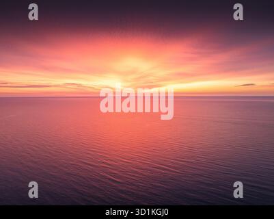 Magnifique coucher de soleil sur la mer ou voir le lever du soleil sur l'eau de l'océan calme au crépuscule avec la surface réfléchissante ondulée des vagues rouges et orange, vue aérienne Banque D'Images