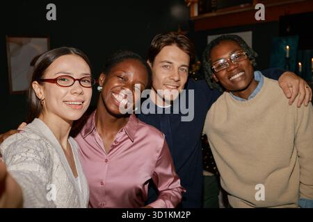 Groupe de jeunes amis multiethniques souriant et posant pour Selfie à l'intérieur Banque D'Images