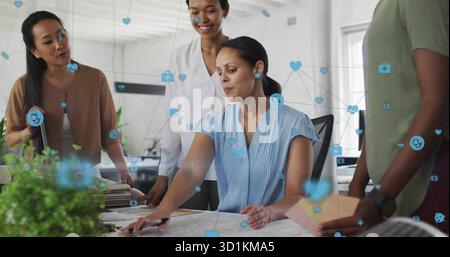 Collaborant femme adulte moyenne écrivant sur des plans dans le bureau ouvert, avec des icônes numériques flottantes Banque D'Images