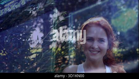 Femme aux cheveux rouges debout portant un haut sans manches blanc dans le jardin avec des panneaux d'interface, espace de copie Banque D'Images