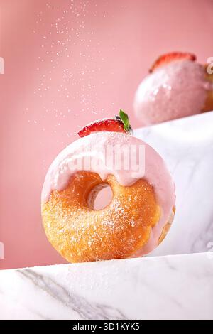Beignet glacé à la fraise avec sucre en poudre et glaçage goutte à goutte sur fond de marbre rose image stock Banque D'Images