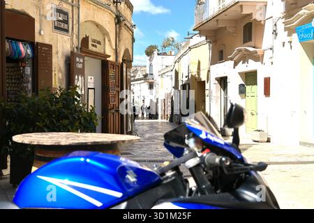 Une étroite ruelle pavée de pierre bordée de bâtiments et de devantures de boutiques dégradés par les intempéries de couleur crème. Portes en bois ouvertes, plantes en pot et balcons encadrent les pas Banque D'Images