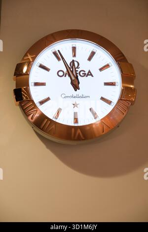 L'horloge de la constellation Omega présente un cadran blanc avec des accents dorés et des chiffres romains, élégamment monté sur un mur dans un terminal très fréquenté de l'aéroport de Changi Banque D'Images