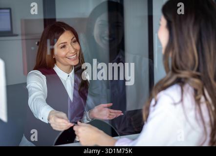 Réceptionniste amicale remettant la carte de membre à la jeune femme et l'accueillant Banque D'Images