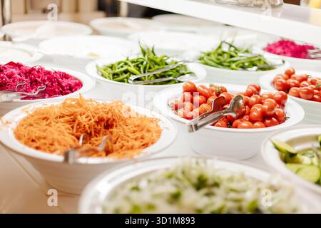 Une variété de légumes frais et de salades sont soigneusement disposés dans des bols lors d'un buffet. Les ingrédients colorés comme les carottes, les tomates et les légumes verts invitent les gues Banque D'Images