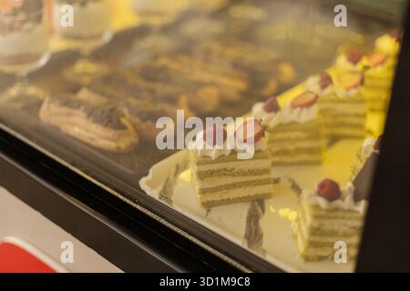 De délicieux gâteaux et pâtisseries superposés sont magnifiquement disposés dans une vitrine de boulangerie. Chaque friandise présente des décorations uniques, attirant les clients w Banque D'Images