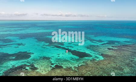 Vue aérienne d'un bateau solitaire flottant sur des eaux turquoises, révélant les motifs complexes des fonds marins, une danse de lumière et d'ombre, Key West, Floride Banque D'Images