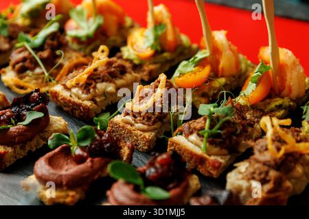 Gros plan de canapés assortis garnis de viande hachée, de crevettes, de tomates, d'herbes et de tartinade servis sur des tranches de pain. Banque D'Images