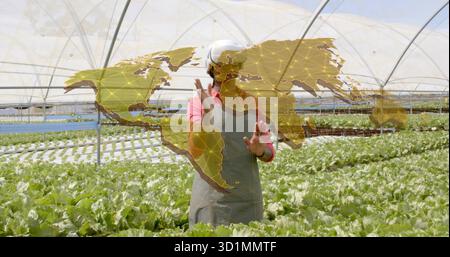 Femme portant la visière du casque faisant des gestes à la carte holographique à l'intérieur de la serre, avec des auges de laitue Banque D'Images