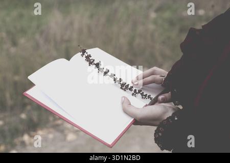 Une jeune femme tient un journal ouvert dans lequel une branche d'herbe est incrustée. Ambiance rétro en automne. La nostalgie est une image tonique dans la nature Banque D'Images