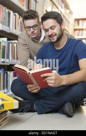 Deux amis, jeunes étudiants collaborant sur le projet en bibliothèque Banque D'Images