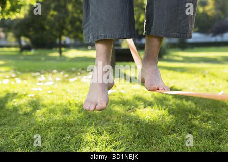 Gros plan des pieds d'homme équilibrant une corde serrée ou slackline dans un environnement de parc avec un pied au-dessus de la corde Banque D'Images
